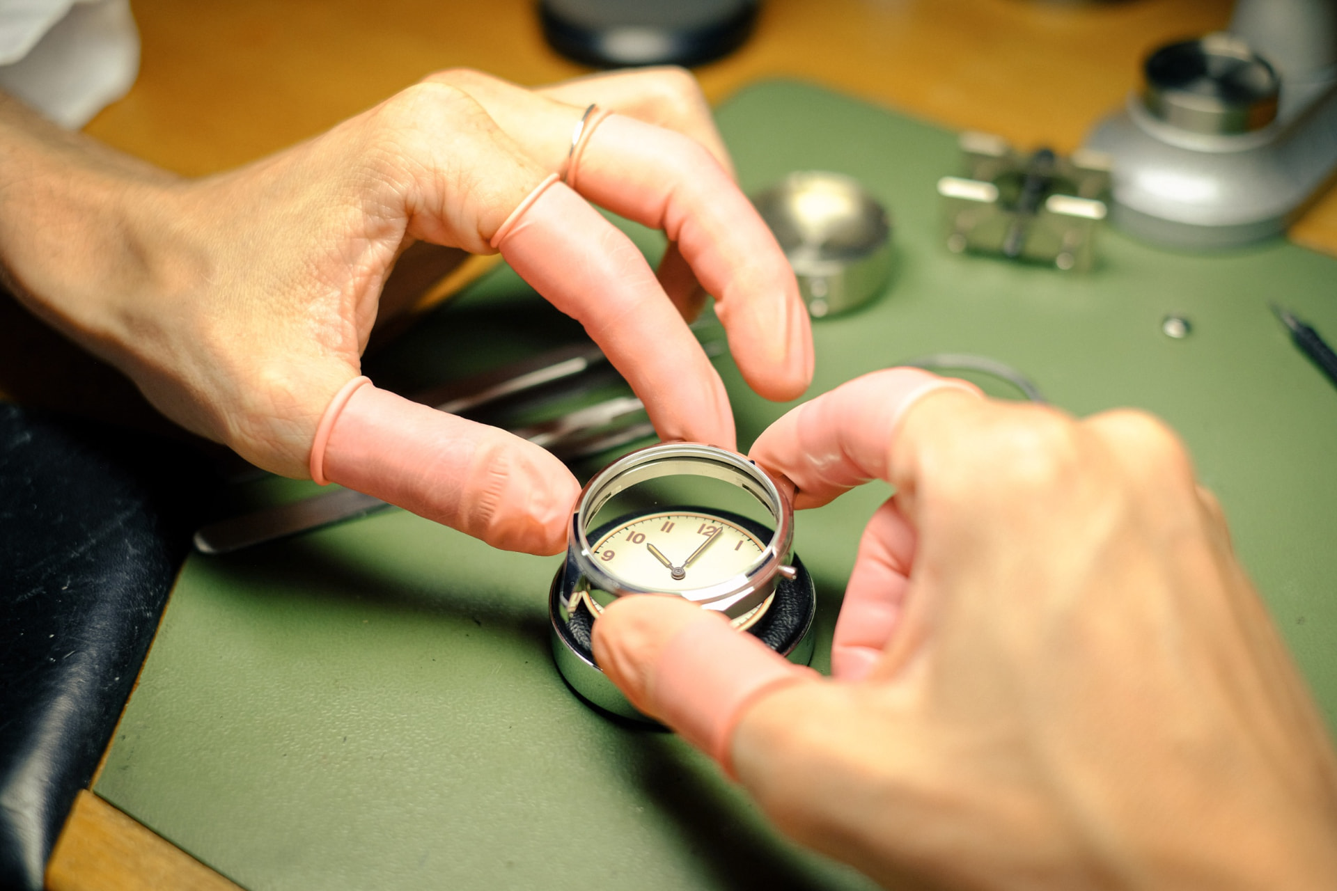 Watchmaker's hands fitting the crystal onto a watch case at the bench